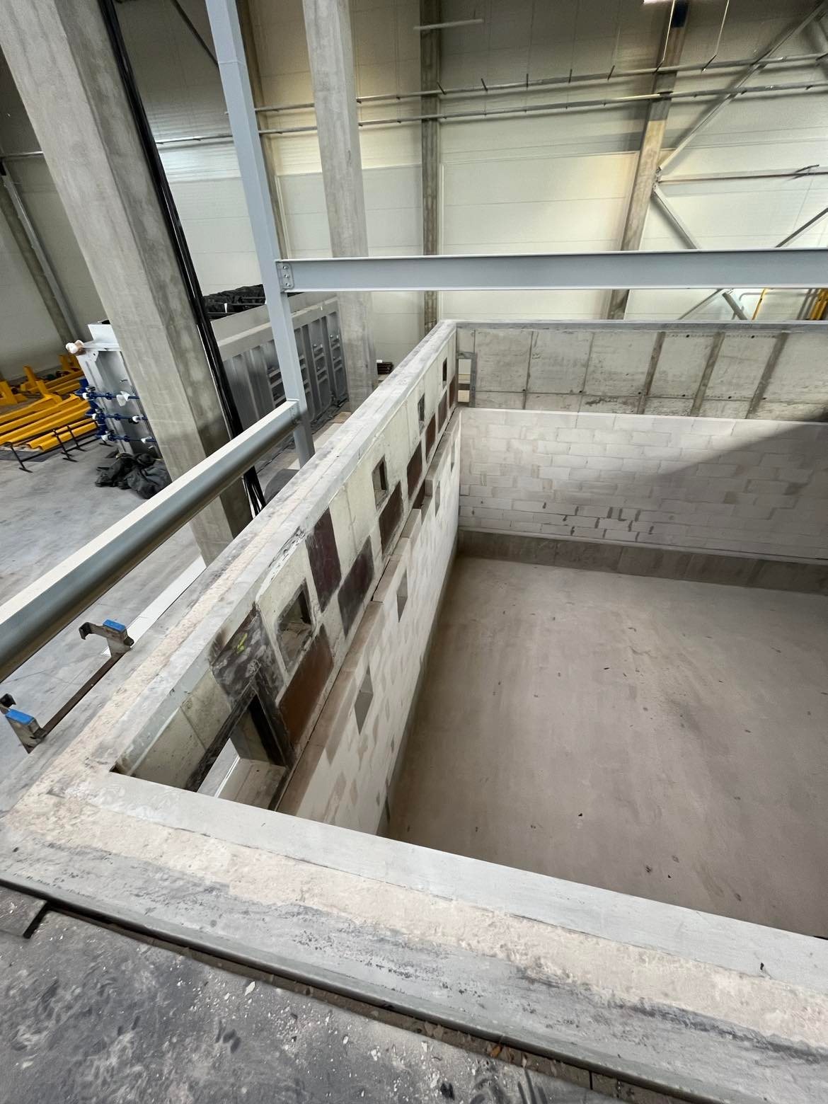 Surowa konstrukcja z betonu komórkowego w hali produkcyjnej z widocznymi otworami w ścianie, wsparta na stalowych belkach i betonowych kolumnach.