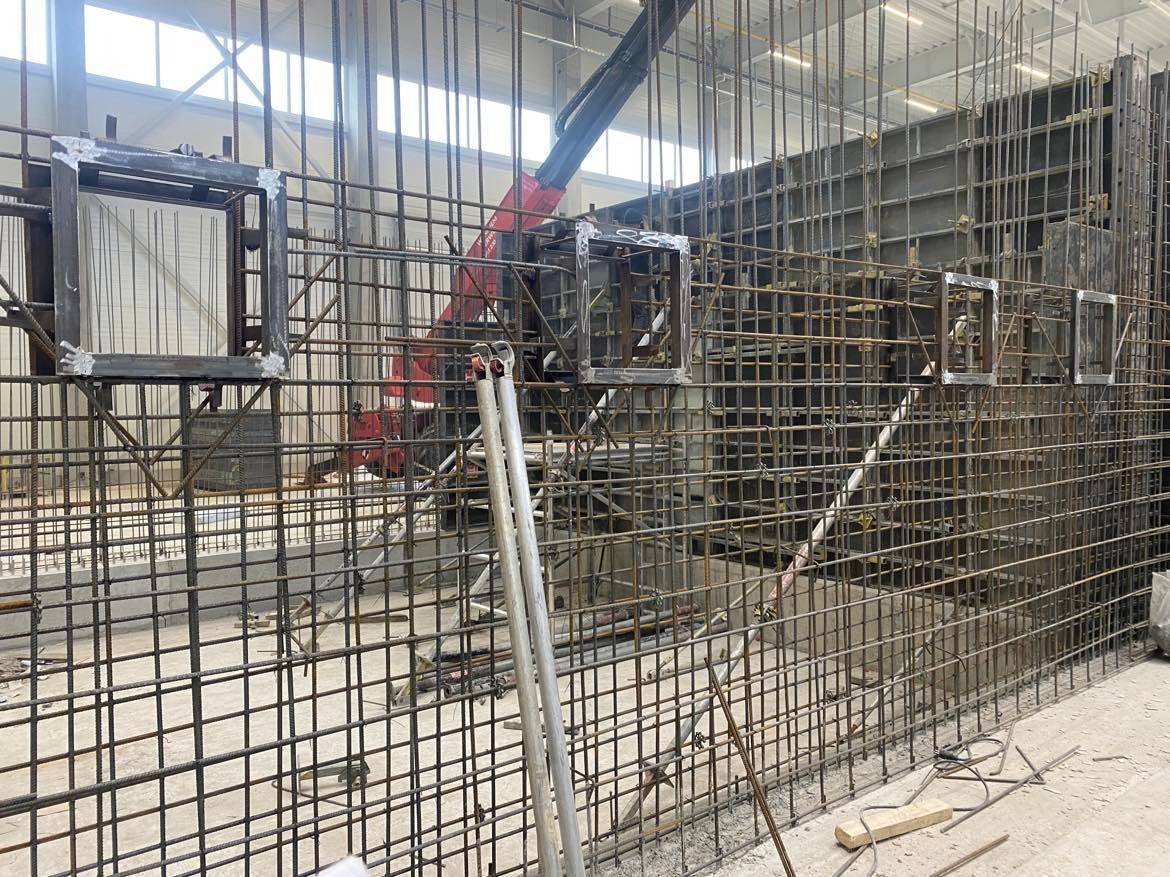 Konstrukcja zbrojeniowa z metalowymi ramkami i widocznym żurawiem w tle, przygotowana do zalewania betonem.