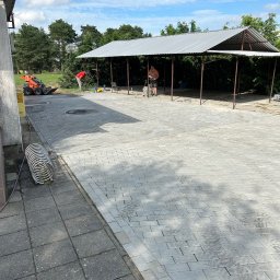 DRBRUK - Układanie szarej kostki brukowej na posesji, widoczny mini-ładowarka i pracownicy w trakcie robót.