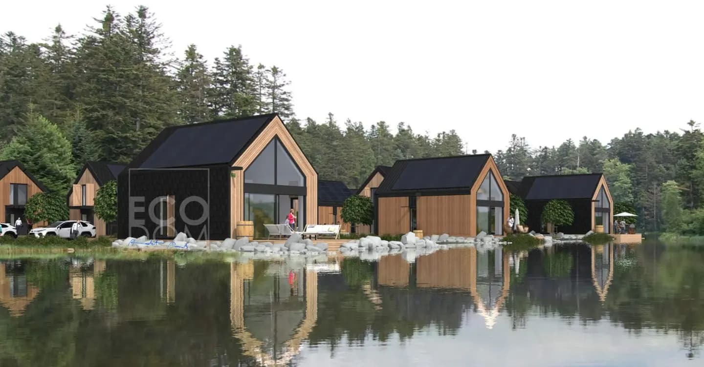 Wizualizacja osady domków z drewna nad jeziorem, z czarnymi dachami i elementami elewacji. Na pierwszym planie tafla wody odbijająca budynki i drzewa.