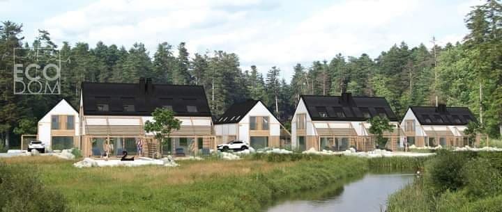 Wizualizacja osiedla domów szkieletowych z czarnymi dachami i jasną elewacją, położonych nad rzeką, z widocznym logo 'ECO DOM' na jednym z budynków.