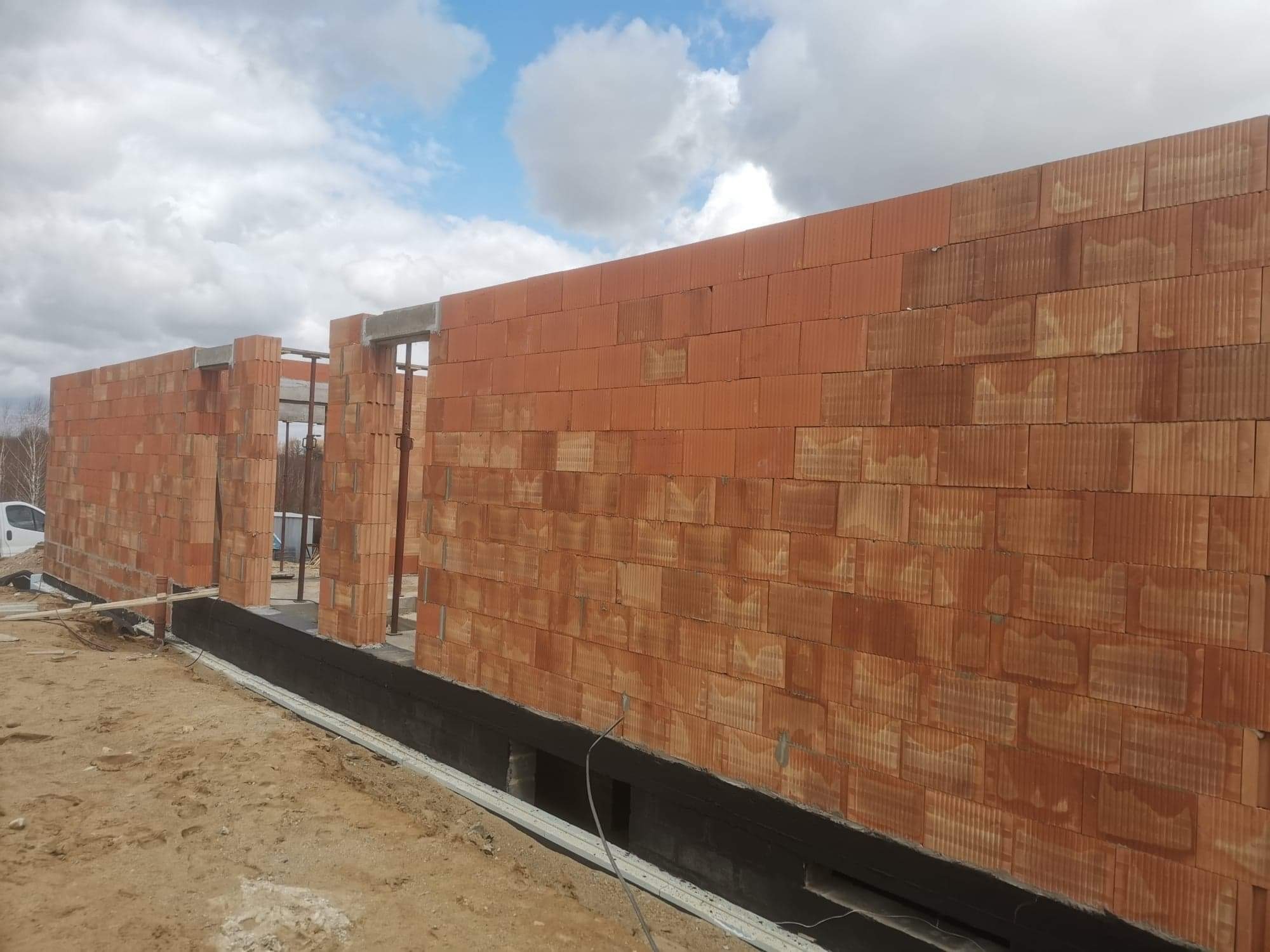 Murowanie ścian z czerwonej cegły ceramicznej w Nowym Mieście Lubawskim, widoczne zbrojenie i izolacja fundamentów, etap budowy domu.