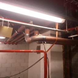 mart spaw - Instalacja rur w budynku w Woli Murowanej. Widoczne rury miedziane, stalowe i elementy mocujące pod sufitem. Prace spawalnicze w trakcie realizacji.