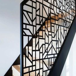 mart spaw - Nowoczesna balustrada schodowa z czarnej stali, o geometrycznym wzorze, zamontowana przy drewnianych schodach w jasnym wnętrzu. Minimalistyczny design.