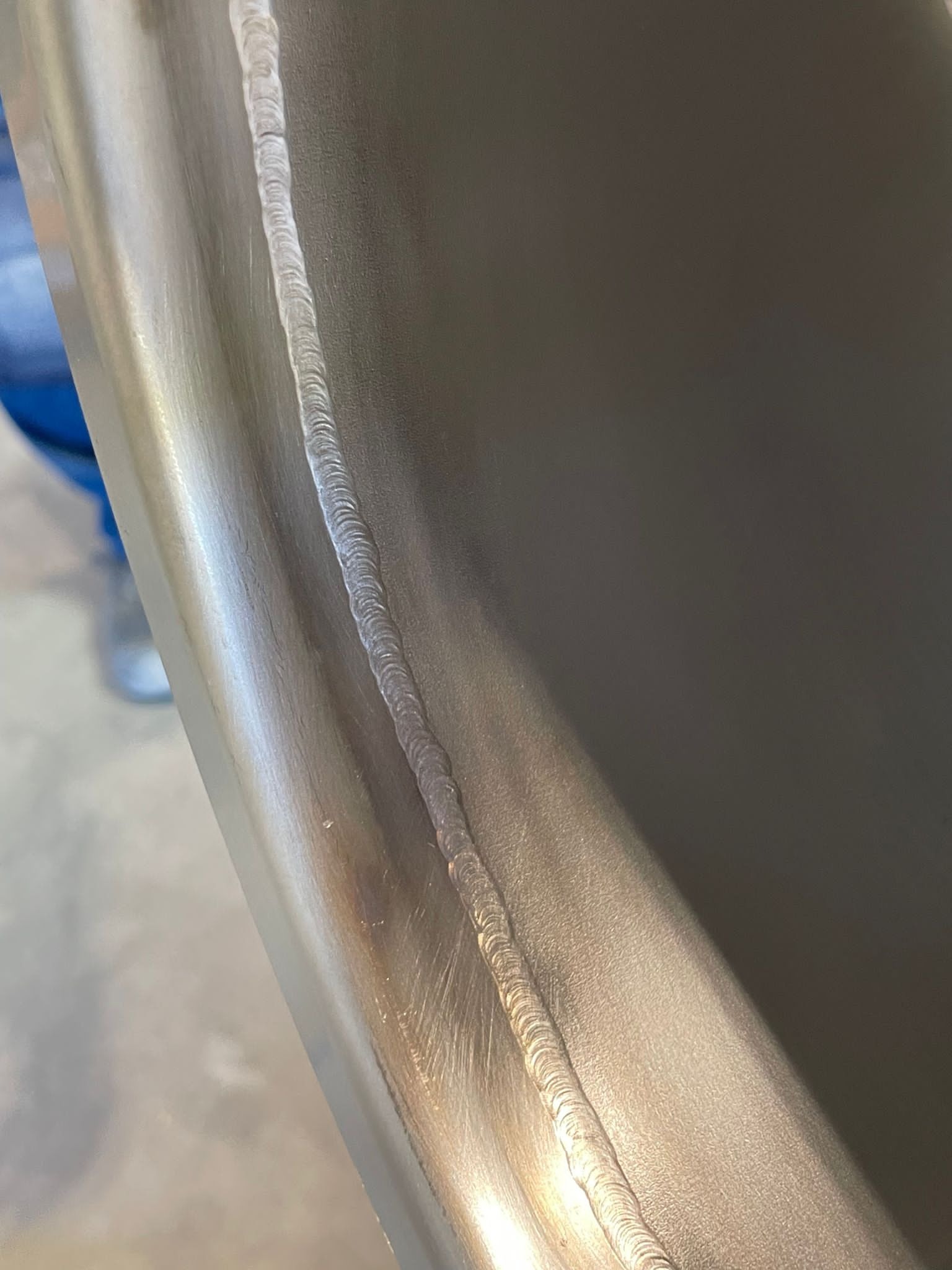 Metalowa powierzchnia z wyraźnym, równym spoiwem spawalniczym biegnącym wzdłuż krawędzi. Widoczne ślady obróbki i delikatne refleksy światła na metalu.