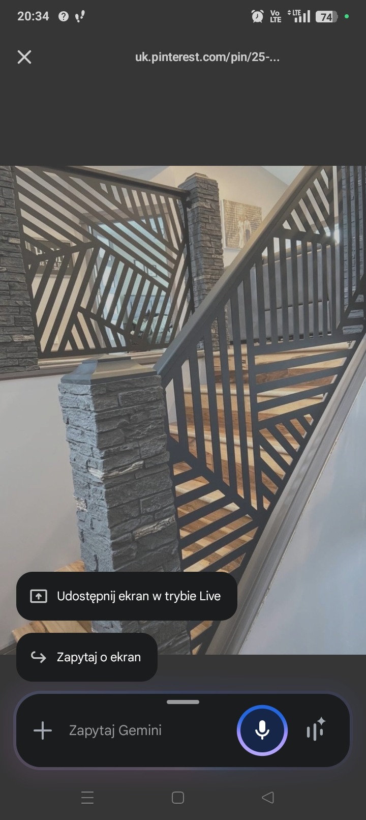 Nowoczesna balustrada schodowa z metalu o geometrycznym wzorze, z kamiennymi słupkami. Ujęcie z dołu schodów, ukazujące detale konstrukcji i wykończenia.