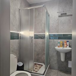 PHU ROBÓT BUDOWLANYCH A. PALUCH - Szara łazienka z kabiną prysznicową, umywalką i toaletą. Ściany wyłożone płytkami imitującymi beton, z dekoracyjnym pasem zielonych płytek. Nowoczesne oświetlenie LED.