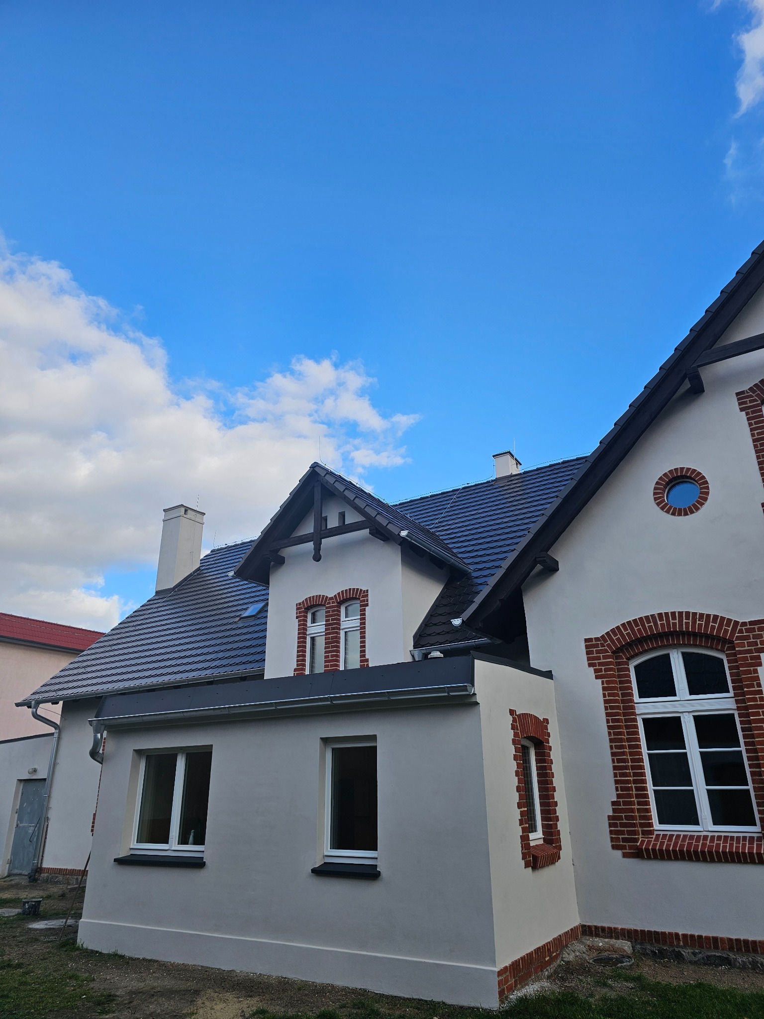 Odnowiona elewacja budynku z elementami dekoracyjnymi z cegły, widok z dołu na tle błękitnego nieba z chmurami.