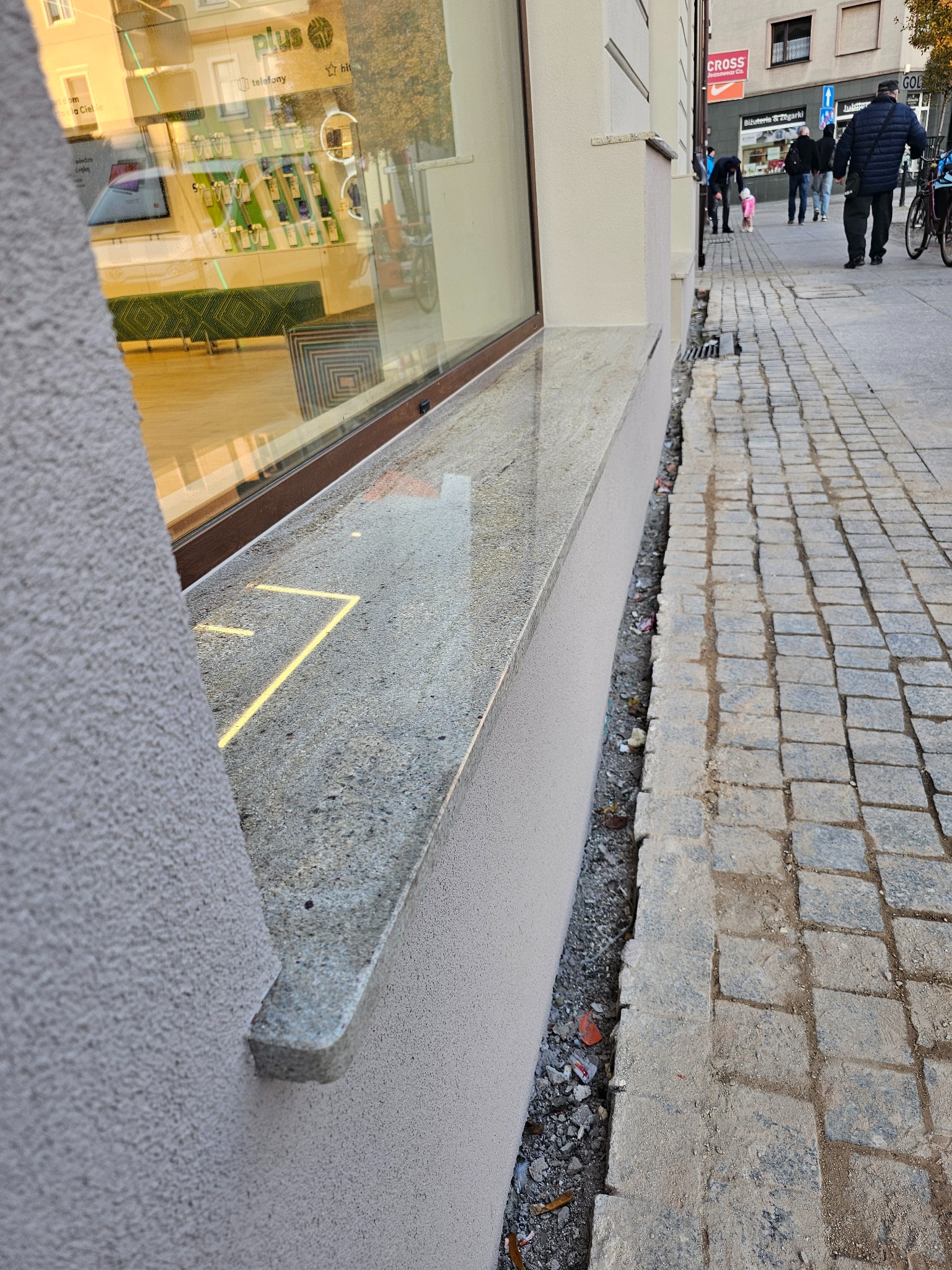 Elewacja budynku z nowym, granitowym parapetem okiennym, widok z poziomu chodnika. Detal wykończenia, szara kolorystyka, kostka brukowa.