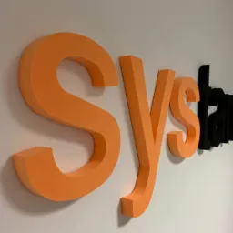 Pomarańczowe i czarne trójwymiarowe litery tworzące napis na białej ścianie, widoczne pod kątem.