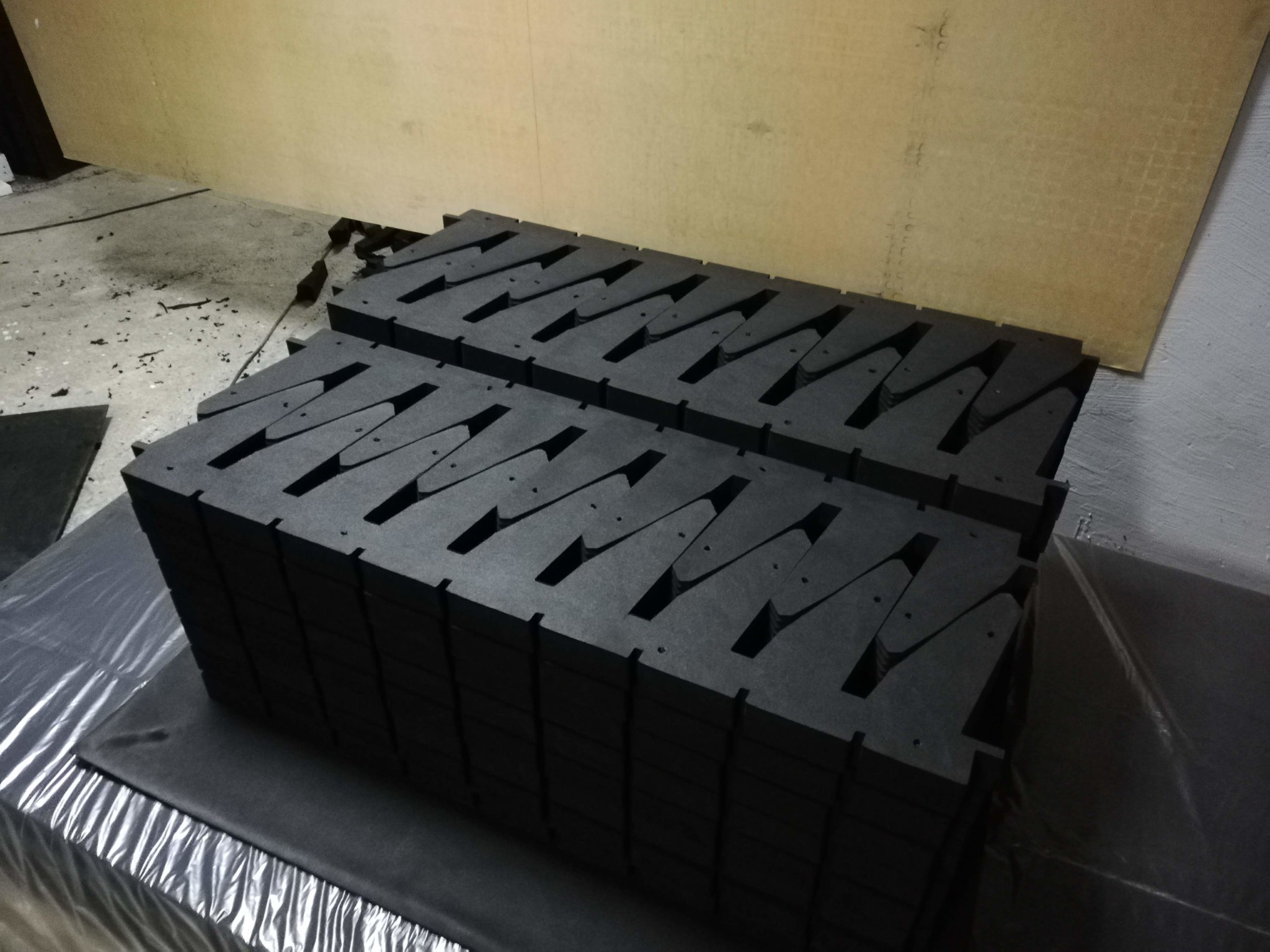 Stos czarnych, piankowych wkładek z wyciętymi otworami, ułożonych na folii ochronnej w magazynie.