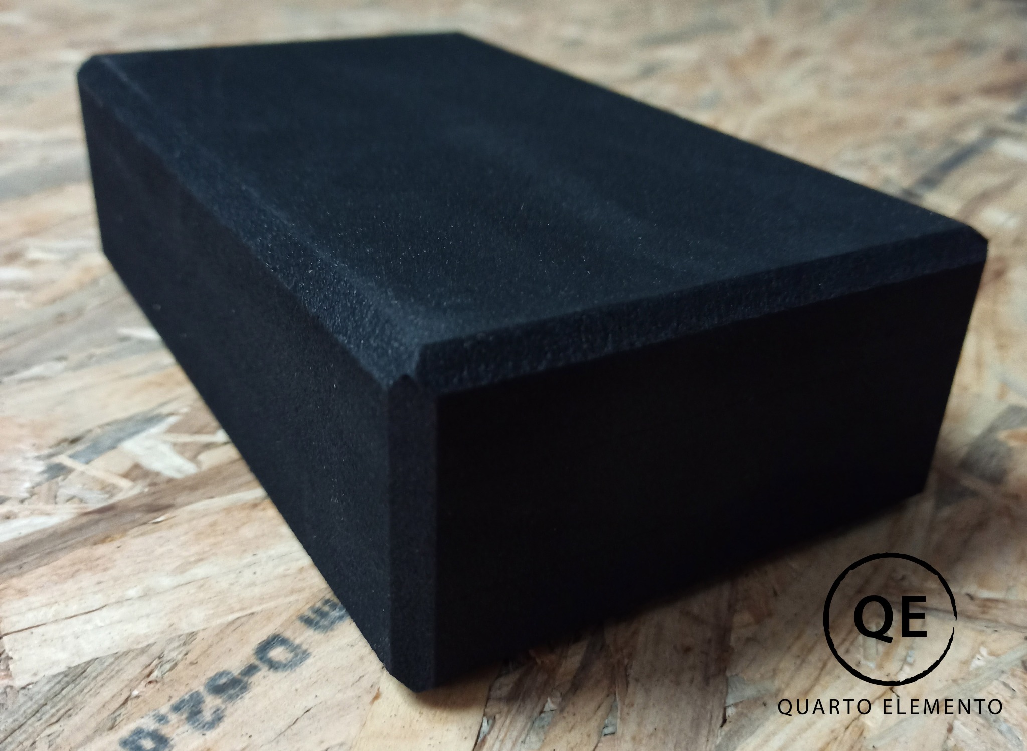Czarny, prostopadłościenny element z zaokrąglonymi krawędziami, przypominający piankowy blok, umieszczony na płycie OSB z widocznym logo firmy Quarto Elemento.