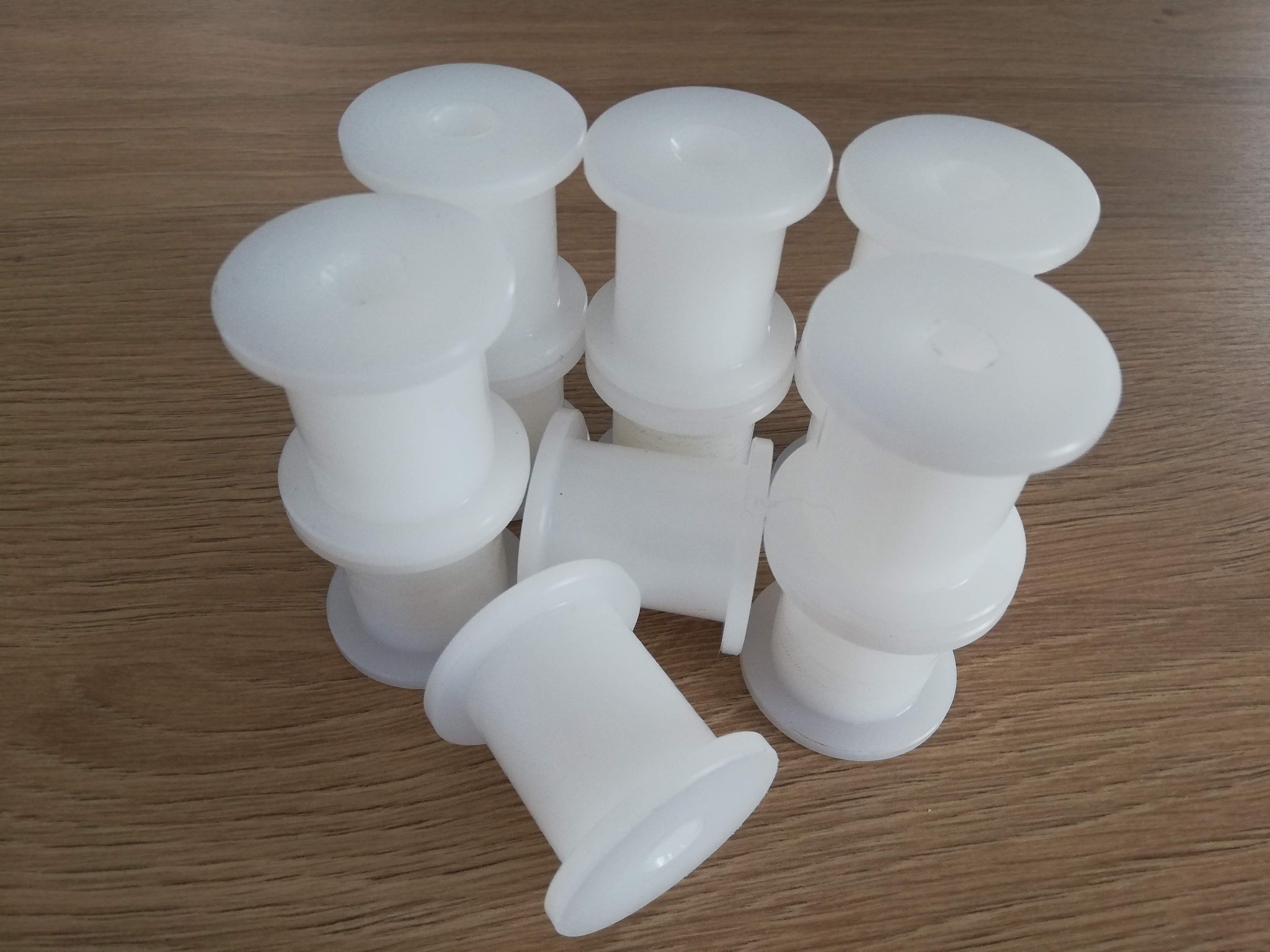 Białe, plastikowe szpule na drewnianym blacie, ułożone w stos z jedną szpulą leżącą bokiem.