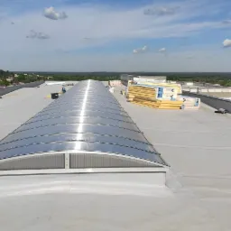 Montaż świetlika tunelowego na dachu płaskim, widoczne panele izolacyjne i narzędzia, w tle krajobraz z zielenią i błękitnym niebem.