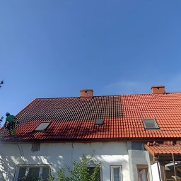 Wash Expert - Częściowo wyczyszczony dach z czerwonej dachówki podczas pracy. Widoczna różnica w kolorze między czystą a brudną częścią dachu. Pracownik w zielonym kombinezonie.