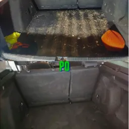 Bagażnik samochodu osobowego przed i po czyszczeniu, widoczne pozostałości po liściach i piasku na dywaniku przed czyszczeniem, a po czyszczeniu dywanik czysty i odkurzony, żółta kamizelka...