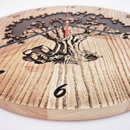 SAMSON Mariusz Samson - Okrągły zegar z jasnego drewna z wygrawerowanym motywem drzewa i cyframi, wskazówki czarne i czerwona, widoczne słoje drewna.