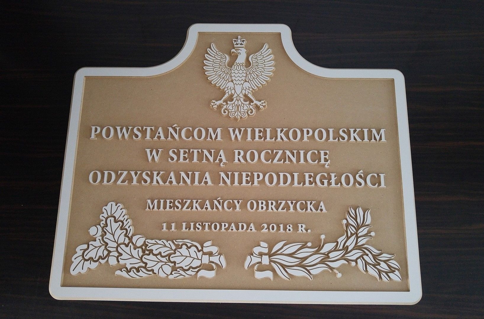 Pamiątkowa tablica z wygrawerowanym tekstem 'POWSTAŃCOM WIELKOPOLSKIM W SETNĄ ROCZNICĘ ODZYSKANIA NIEPODLEGŁOŚCI MIESZKAŃCY OBRZYCKA 11 LISTOPADA 2018 R.' oraz orłem i motywami roślinnymi...