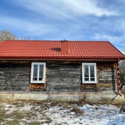 SMARTDACH Sp. z o.o. - Ceglasty blachodach na drewnianym domu z dwoma oknami. Widoczne rynny w kolorze dachu i fragment ośnieżonego terenu. Ujęcie z dołu, podkreślające nową konstrukcję.
