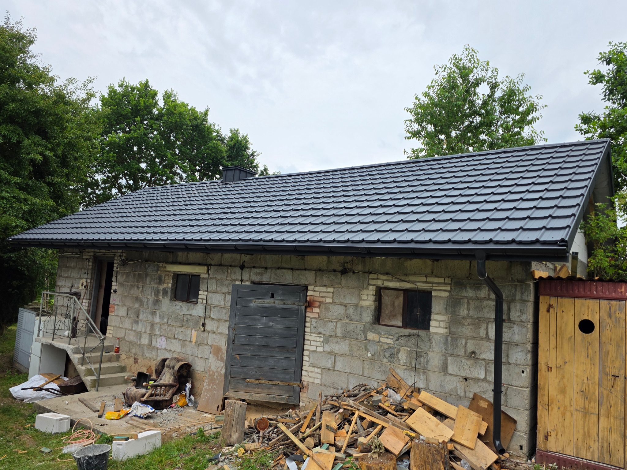 Budynek gospodarczy z nowym, antracytowym dachem z blachodachówki FINN 2.0. Widoczne rynny, podmurowane ściany szczytowe i wylany wieniec. Bodzentyn.