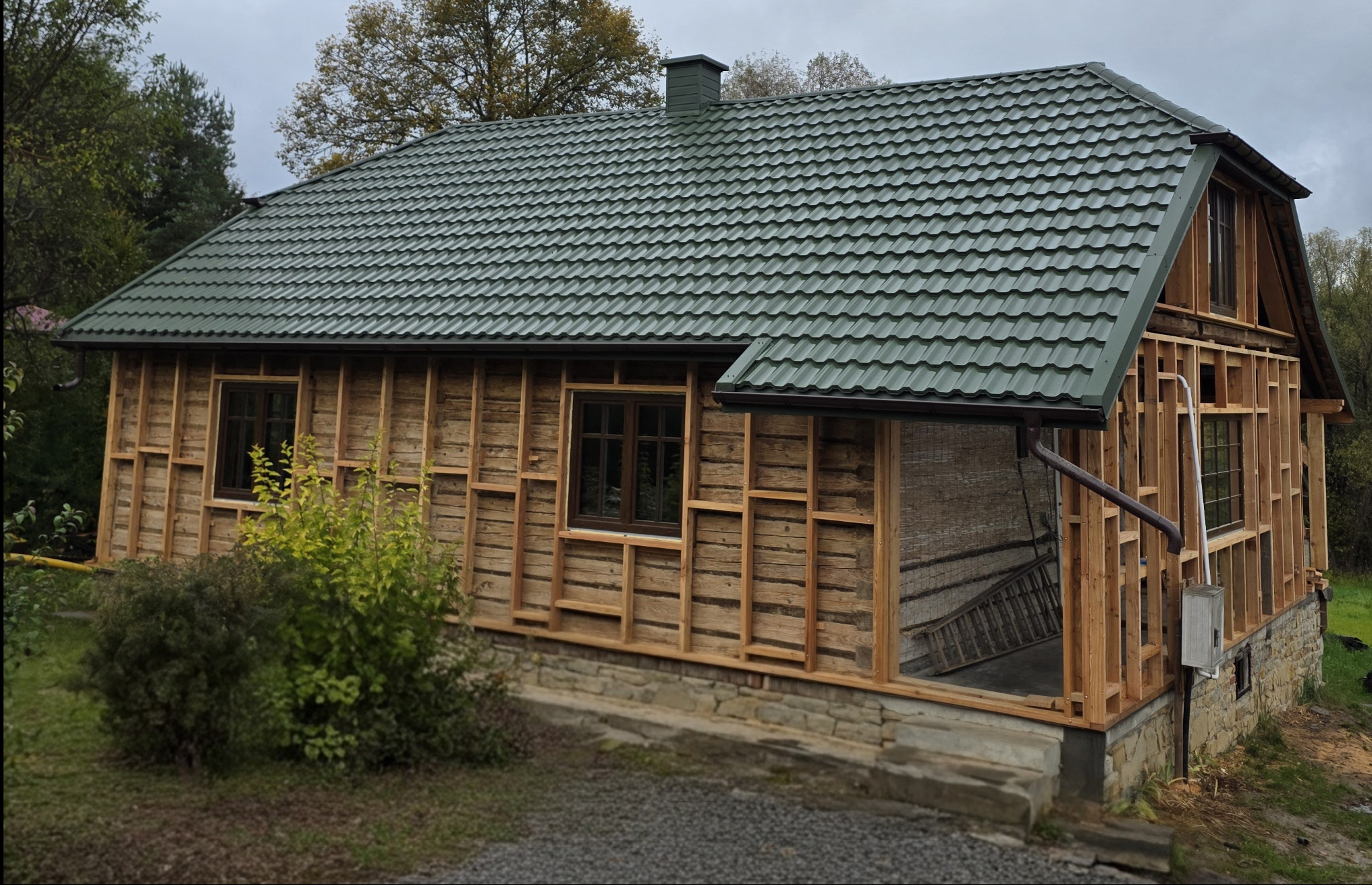 Dom w trakcie wymiany pokrycia dachowego na blachodachówkę GERMAN 6020 PladurWrinkle mat, z metalowymi rynnami BRYZA. Częściowo odsłonięta drewniana konstrukcja ścian.