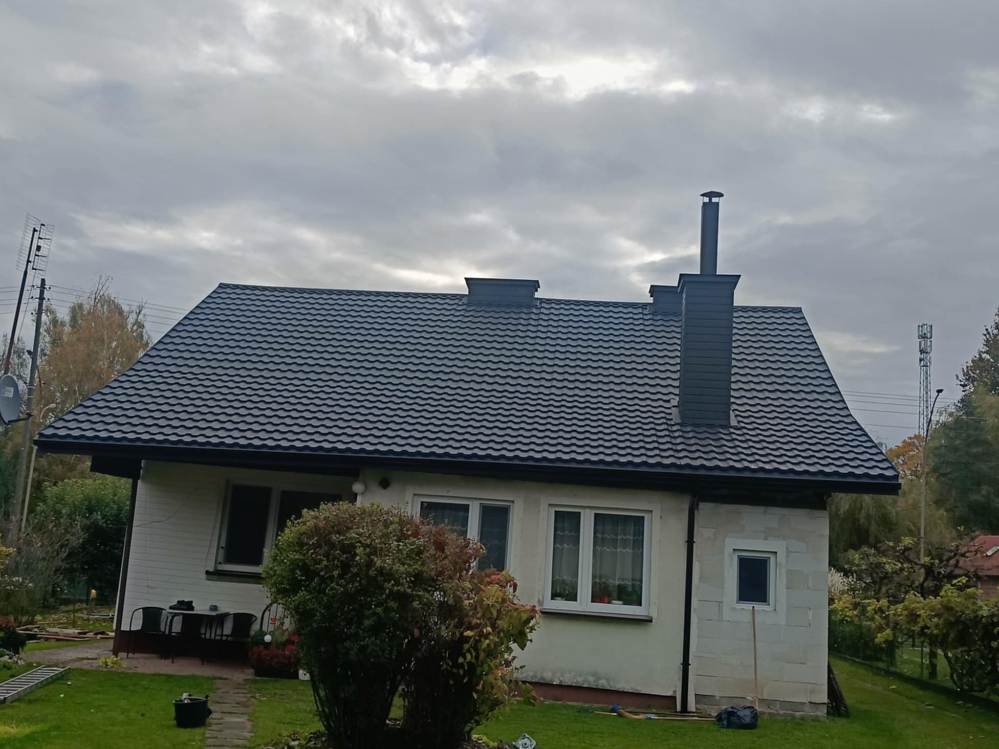 Dom z nowym, grafitowym dachem z blachy trapezowej GERMAN i stalowymi rynnami BRYZA, Oleszyce. Widoczne kominy i fragment ogrodu.
