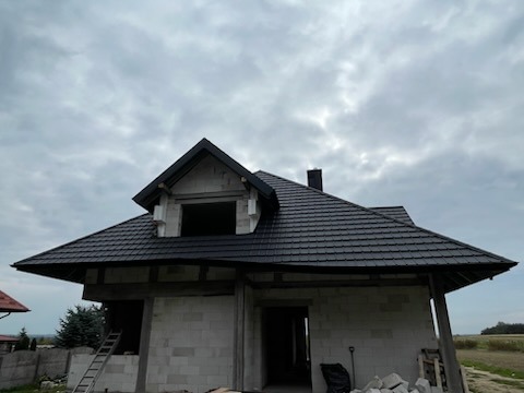 Dom w trakcie budowy z czarnym dachem z blachy DACHPOL PROFUTURA, okna FAKRO i rynny BRYZA. Wólka Niedźwiedzka, pochmurne niebo.