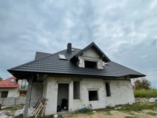 Nowy dach z blachy DACHPOL PROFUTURA 9005 Granite Ultramat, okna FAKRO i stalowe rynny BRYZA na surowym budynku w Wólce Niedźwiedzkiej.