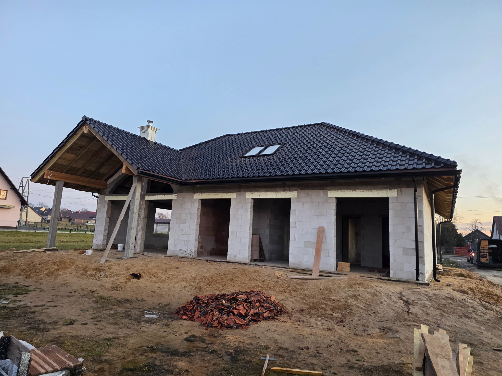Dom w trakcie budowy z czarną, błyszczącą dachówką ceramiczną RÖBEN Milano i metalowymi rynnami BRYZA. Widoczne okna FAKRO i okute kominy.