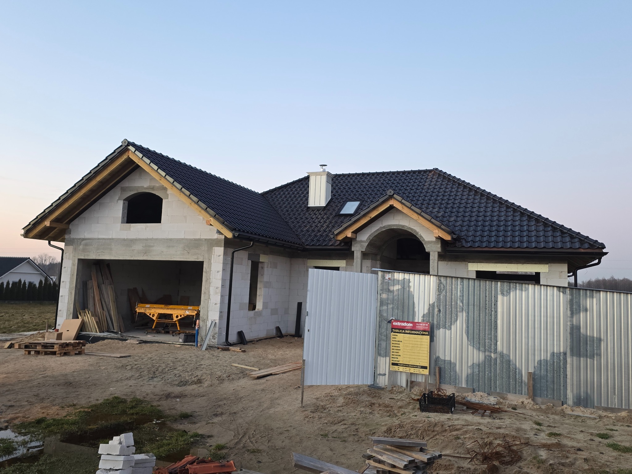 Dom w trakcie budowy z czarną, błyszczącą dachówką ceramiczną RÖBEN Milano i metalowymi rynnami BRYZA. Widoczna więźba dachowa i okute kominy.