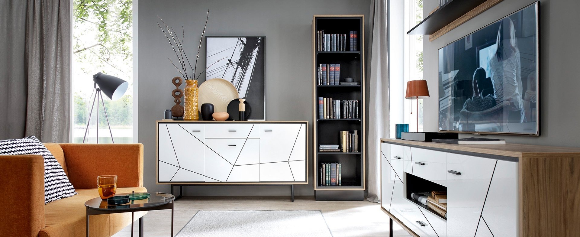 Salon w Elblągu z pomarańczową sofą, stolikiem z napojem, białą komodą z geometrycznym wzorem, regałem z książkami i telewizorem na ścianie.