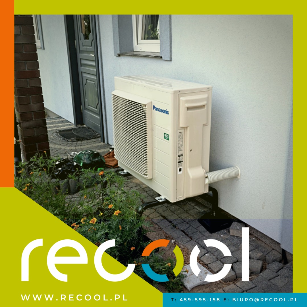 Zewnętrzna jednostka klimatyzacyjna Panasonic zamontowana na czarnym wsporniku przy ścianie budynku z widocznymi elementami instalacji i otaczającą roślinnością; zdjęcie z logo firmy w rogu.