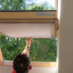 Otwieranie rolety wewnętrznej w oknie dachowym, widok na zieleń za oknem.