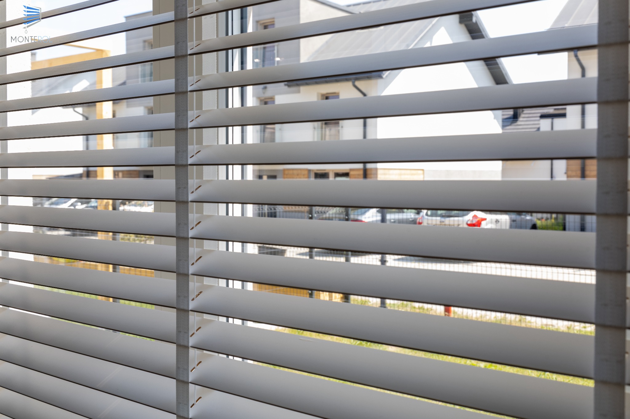 Białe żaluzje drewniane w nowoczesnym domu, widok na ulicę z samochodami i budynkami w tle, delikatne oświetlenie dzienne.