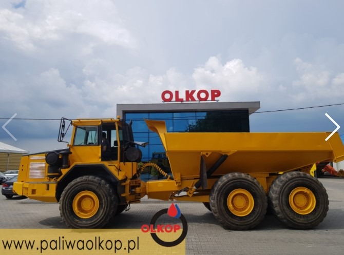 Żółta wywrotka przegubowa na tle budynku z logo OLKOP, widok z boku, na oponach widoczne ślady użytkowania.