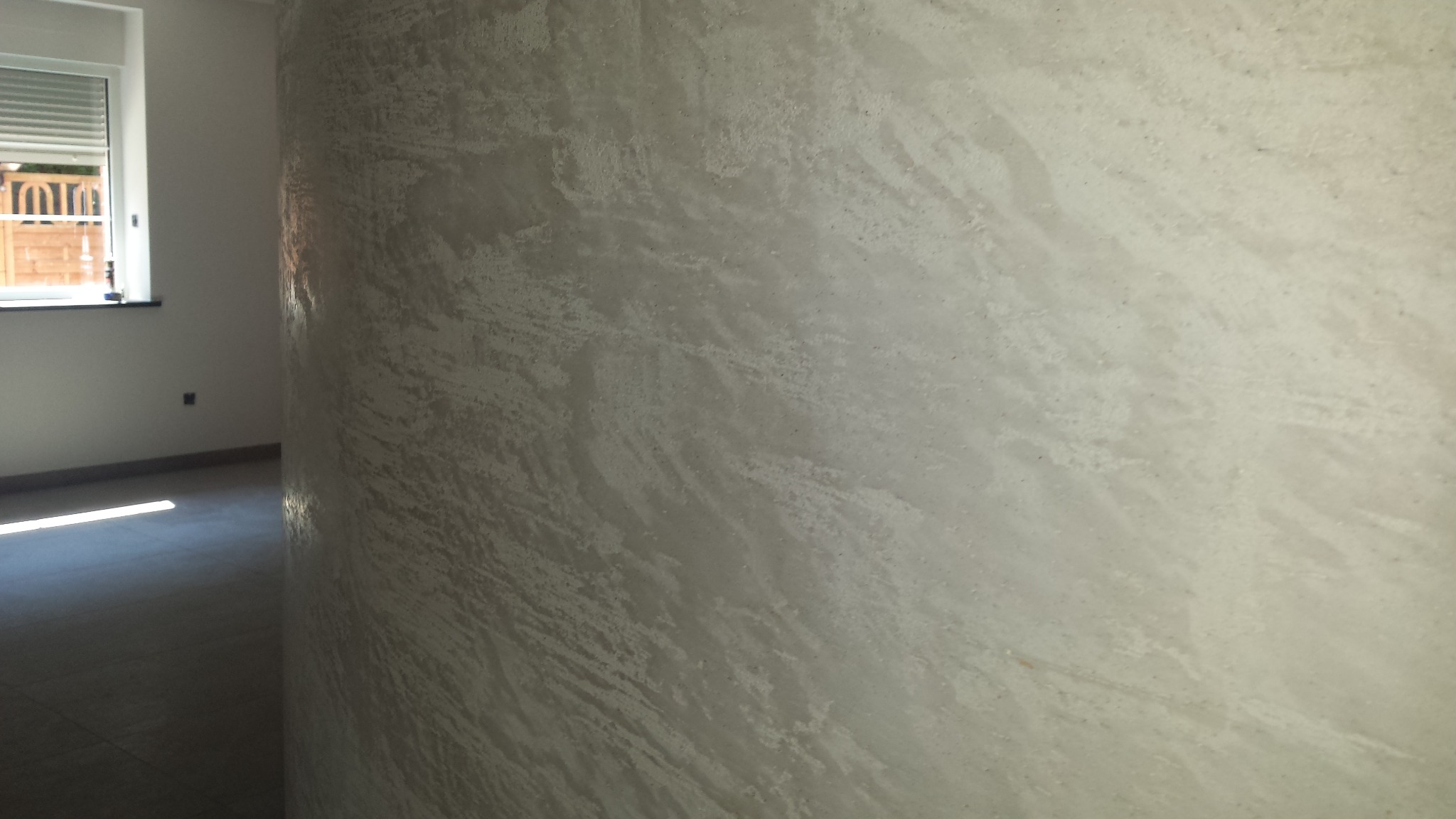 Ściana z efektem dekoracyjnym, imitującym naturalny kamień, w jasnym pomieszczeniu z oknem.