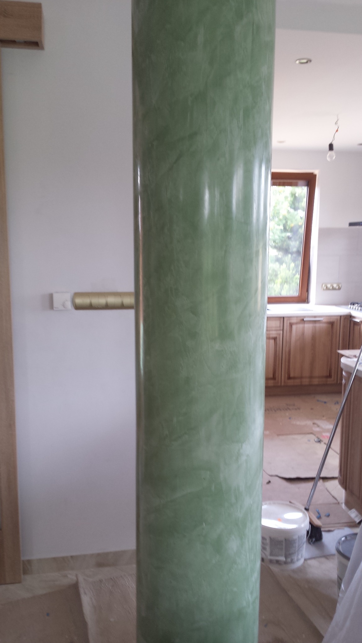 Kolumna w kuchni wykończona techniką stiuk w odcieniach zieleni, widoczne niedokończone prace remontowe w tle.