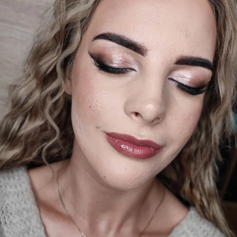 Portret kobiety z zamkniętymi oczami, prezentującej delikatny makijaż oka w odcieniach brązu i różu z wyraźną czarną kreską oraz usta pomalowane błyszczącą pomadką w kolorze mauve.