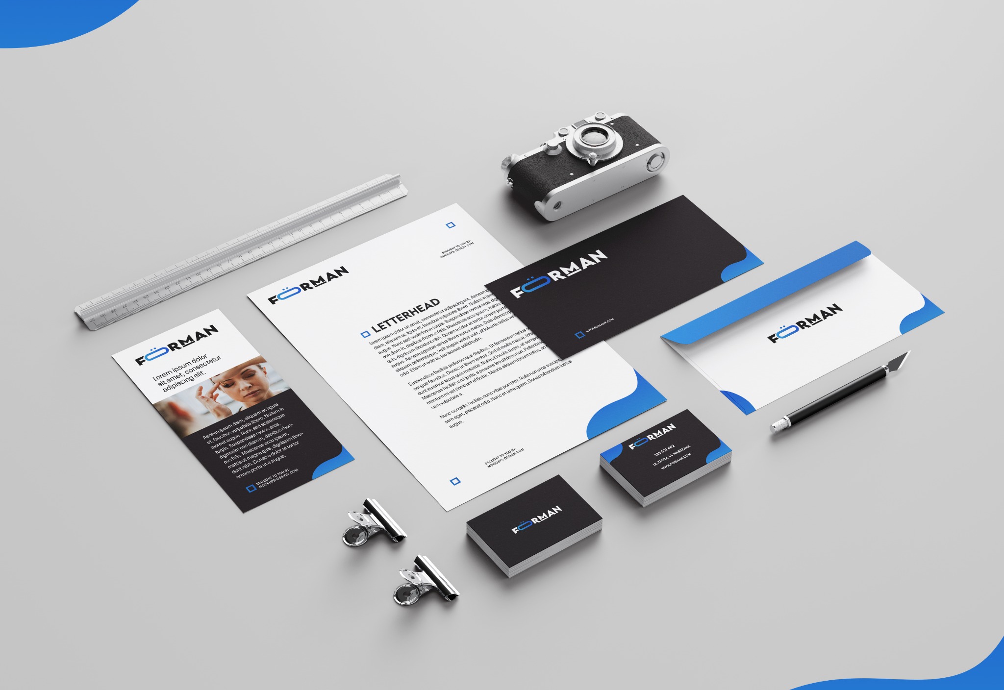 Zestaw materiałów firmowych z logo: wizytówki, papier firmowy, koperta, ulotka, długopis, spinacze i aparat fotograficzny w stylu retro.