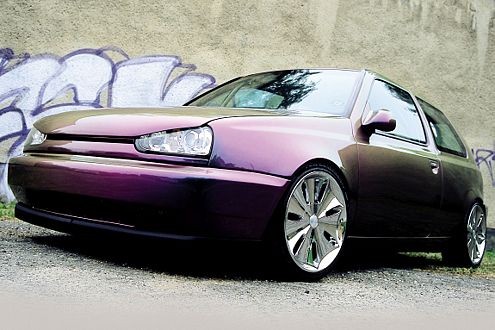 Samochód w kolorze fioletowo-brązowym z chromowanymi felgami na tle ściany z graffiti.