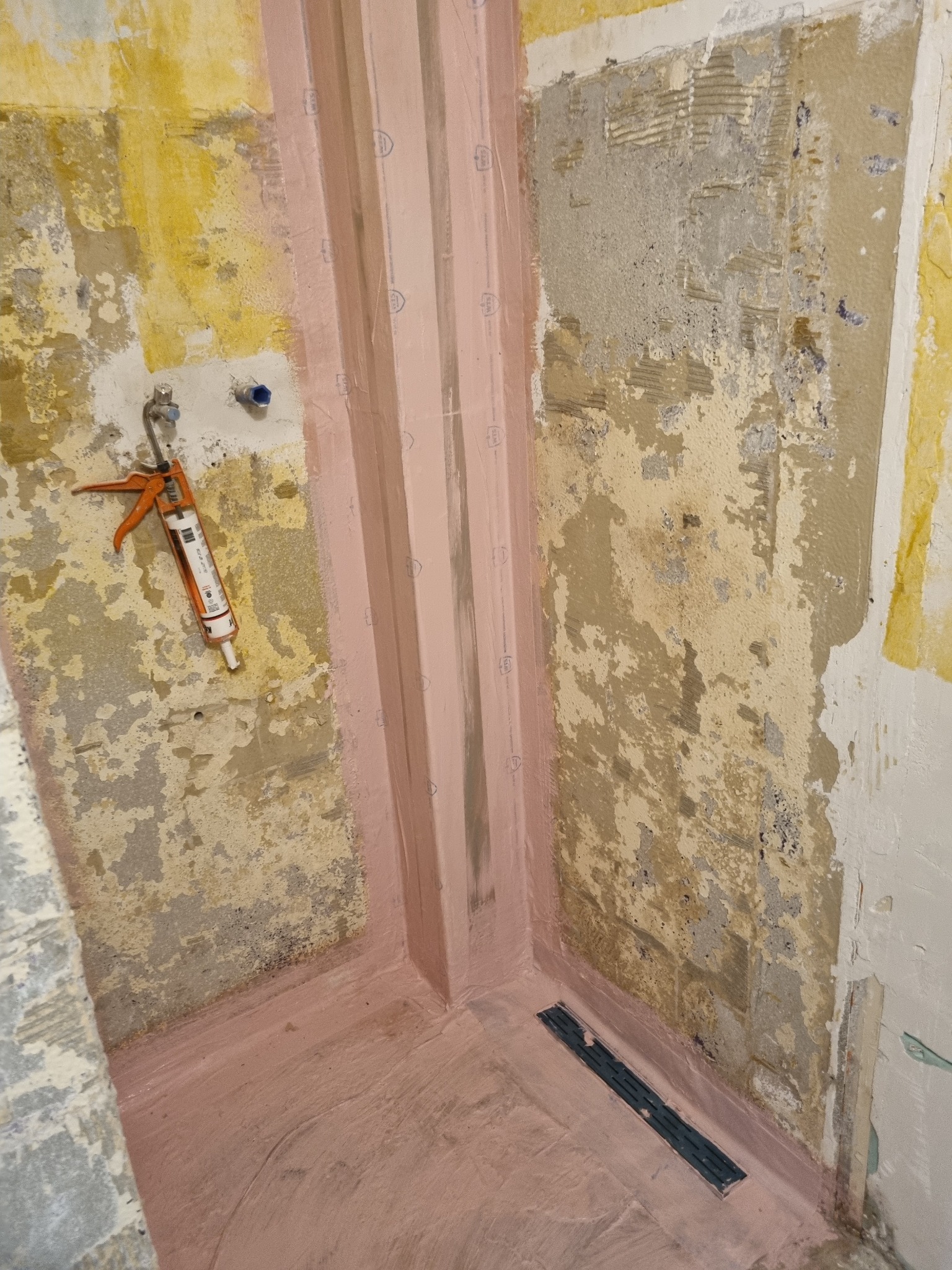 Przygotowanie do hydroizolacji narożnika w łazience z widoczną listwą uszczelniającą, narzędziem do silikonu i odpływem liniowym.