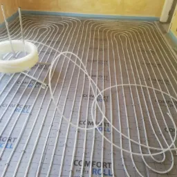 Rozłożone rury ogrzewania podłogowego na izolacji z nadrukiem, widoczny zwój rury i elementy mocujące, przygotowanie do wylewki.