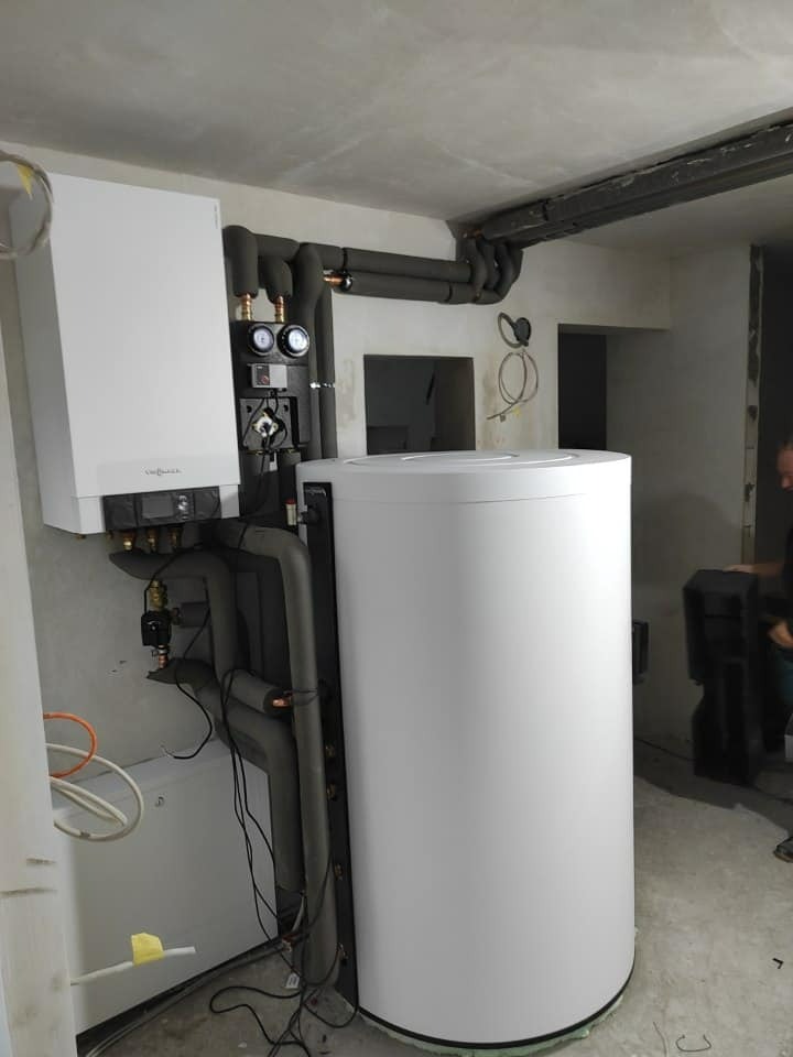 Nowoczesny piec gazowy dwufunkcyjny Viessmann z zasobnikiem ciepłej wody i zaizolowanymi rurami w surowym wnętrzu podczas montażu.