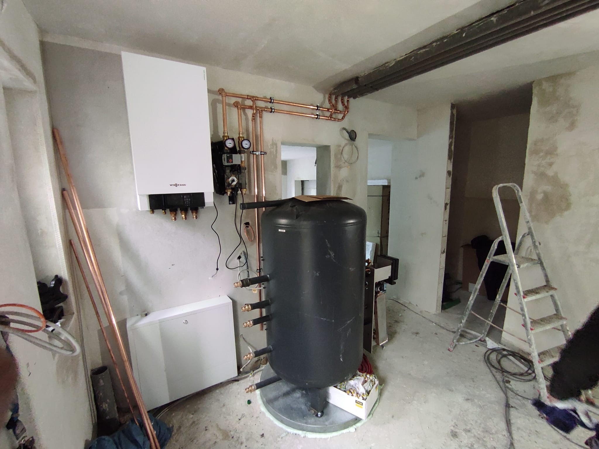 Nowa instalacja grzewcza w surowym wnętrzu: biały piec gazowy Viessmann, czarny zasobnik ciepłej wody, miedziane rury i drabina malarska.