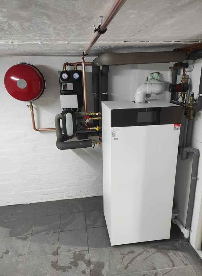 Nowoczesny piec gazowy Viessmann z podłączoną instalacją grzewczą, widoczne rury miedziane, manometry i zawory, zamontowany w pomieszczeniu z szarą podłogą i białymi ścianami.