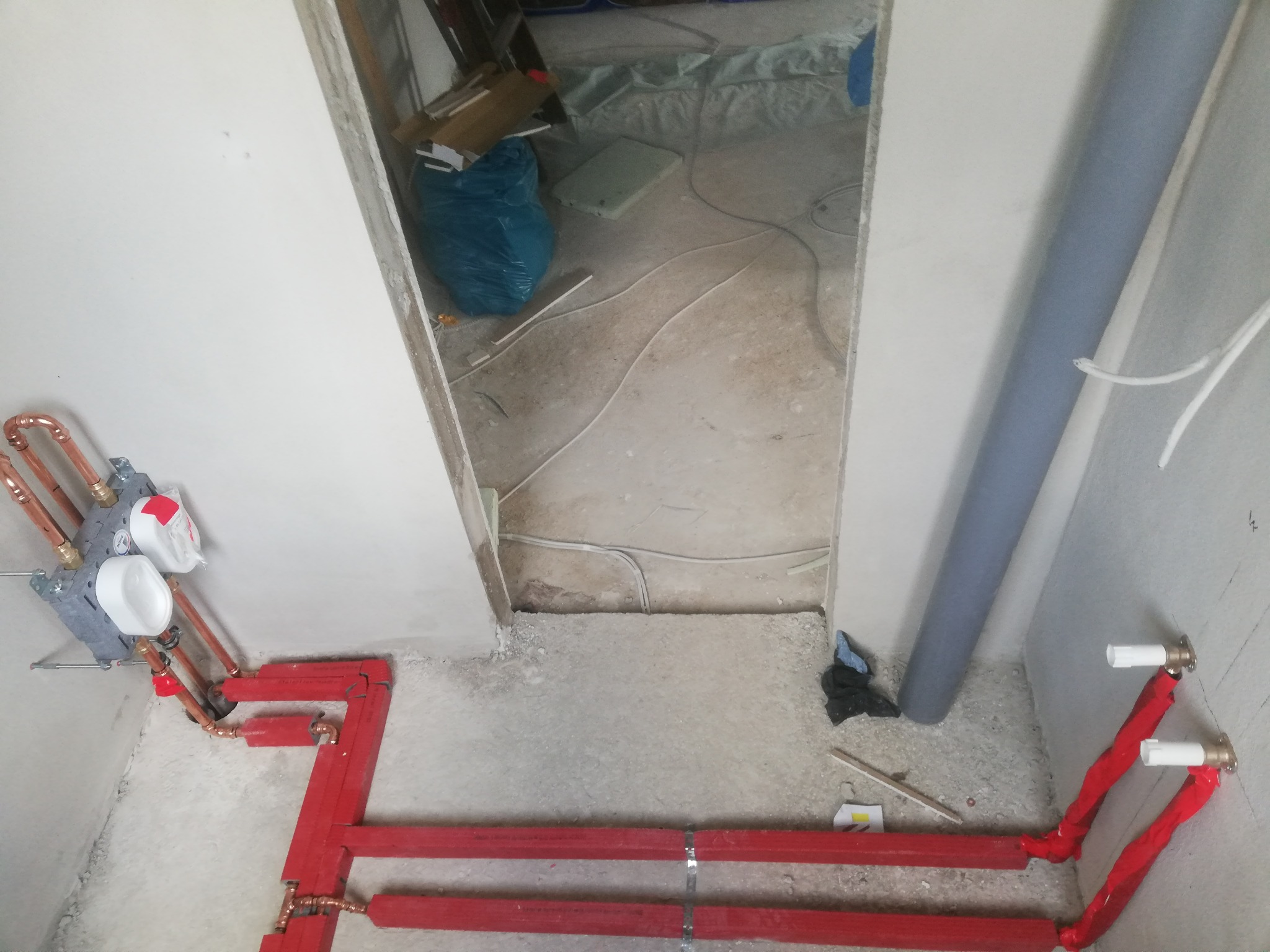 Czerwone rury instalacji grzewczej z miedzianymi złączkami, zamontowane na surowej ścianie w trakcie prac wykończeniowych, widok z góry.