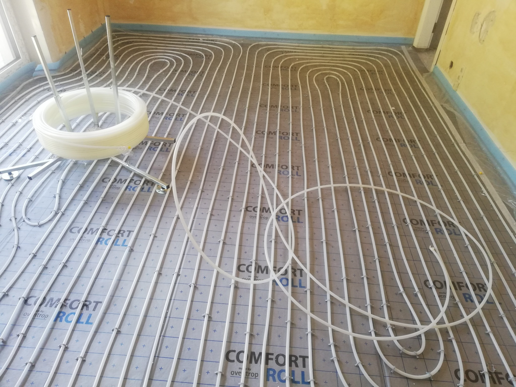 Rozłożone rury ogrzewania podłogowego na izolacji z nadrukiem, widoczny zwój rury i elementy mocujące, przygotowanie do wylewki.