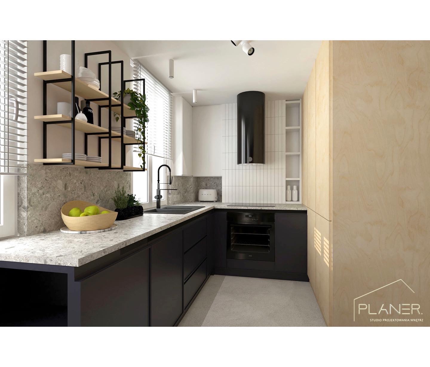 Nowoczesna kuchnia z czarnymi szafkami, blatem z szarego kamienia, wiszącymi półkami z metalu i drewna, oraz okapem w kształcie tuby. Na blacie misa z zielonymi jabłkami i toster Smeg.