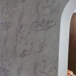 Ściana z efektem marmuru w odcieniach szarości, widoczny fragment czarnego karnisza i zaokrąglone przejście do innego pomieszczenia.