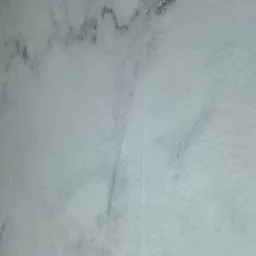 Jasnoszara płytka imitująca marmur z delikatnym, ciemniejszym żyłkowaniem i widoczną fugą.